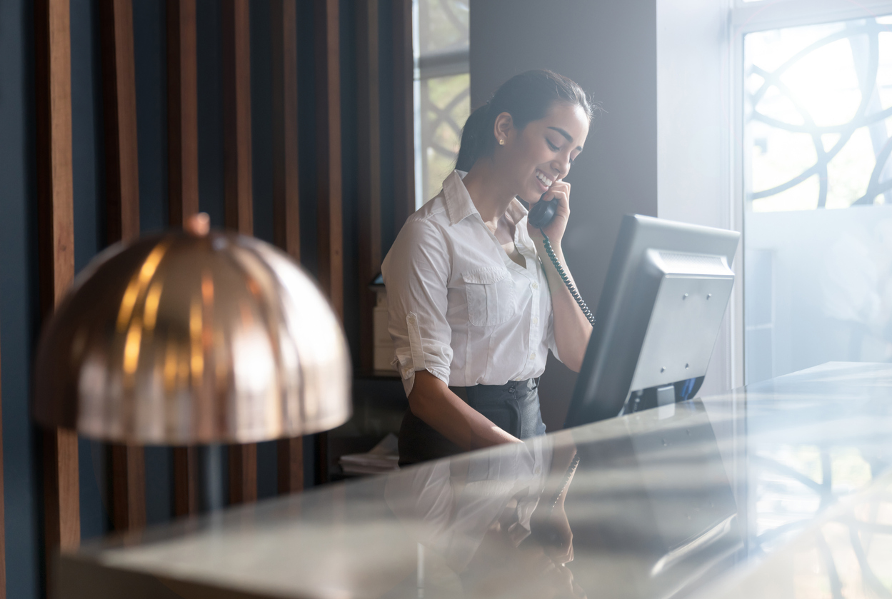 Beautiful friendly hotel receptionist answering a call from a guest smiling very happy