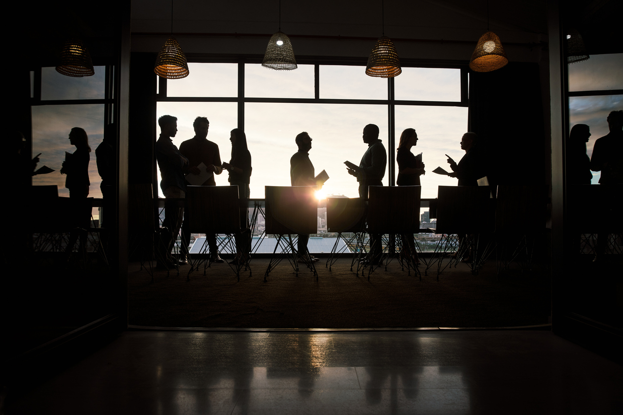 Full length silhouetted shot of a group of businesspeople working and conversing together inside a modern office