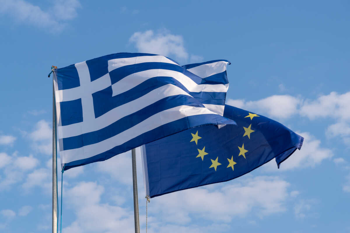 The national flag of Greece and the flag of the European Union fluttering in the wind at the waterfront of Nikiti, Sithonia, Greece.