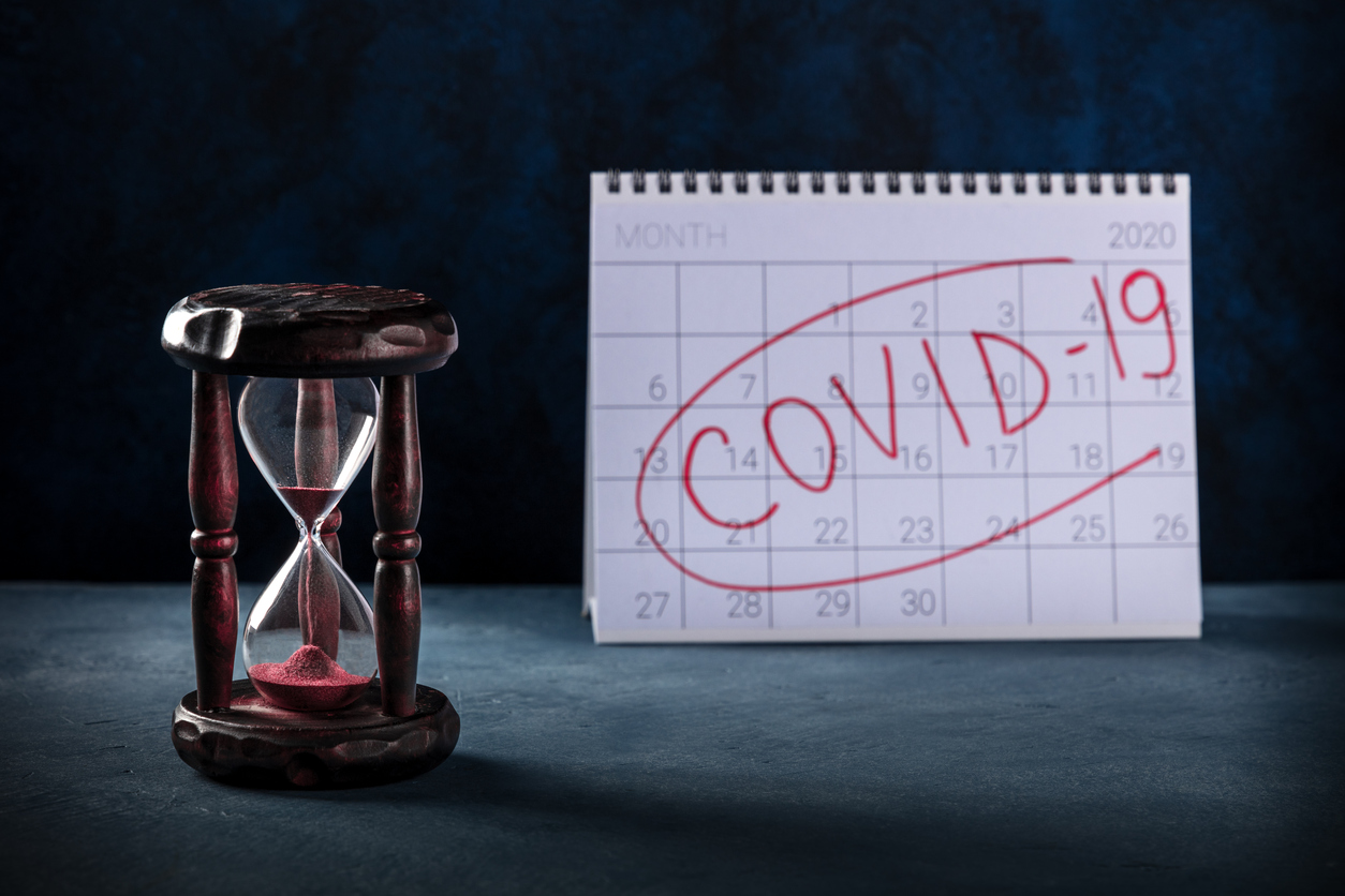 Covid, how long will it last, waiting for the vaccine concept, a monthly calendar for the year 2020 and an hourglass on a dark background