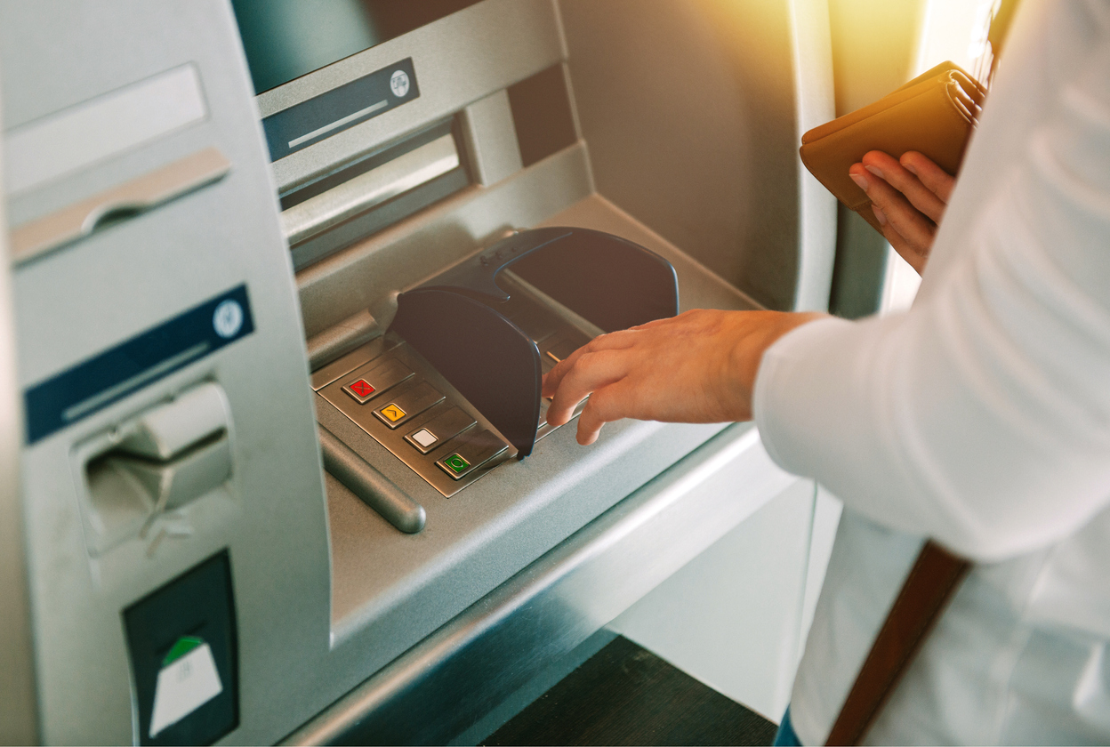 Woman using ATM holding wallet an pressing the PIN security number on the keyboard automatic teller machine