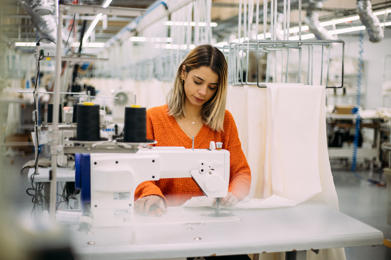Young tailor making clothes with electric sewing machine in factory