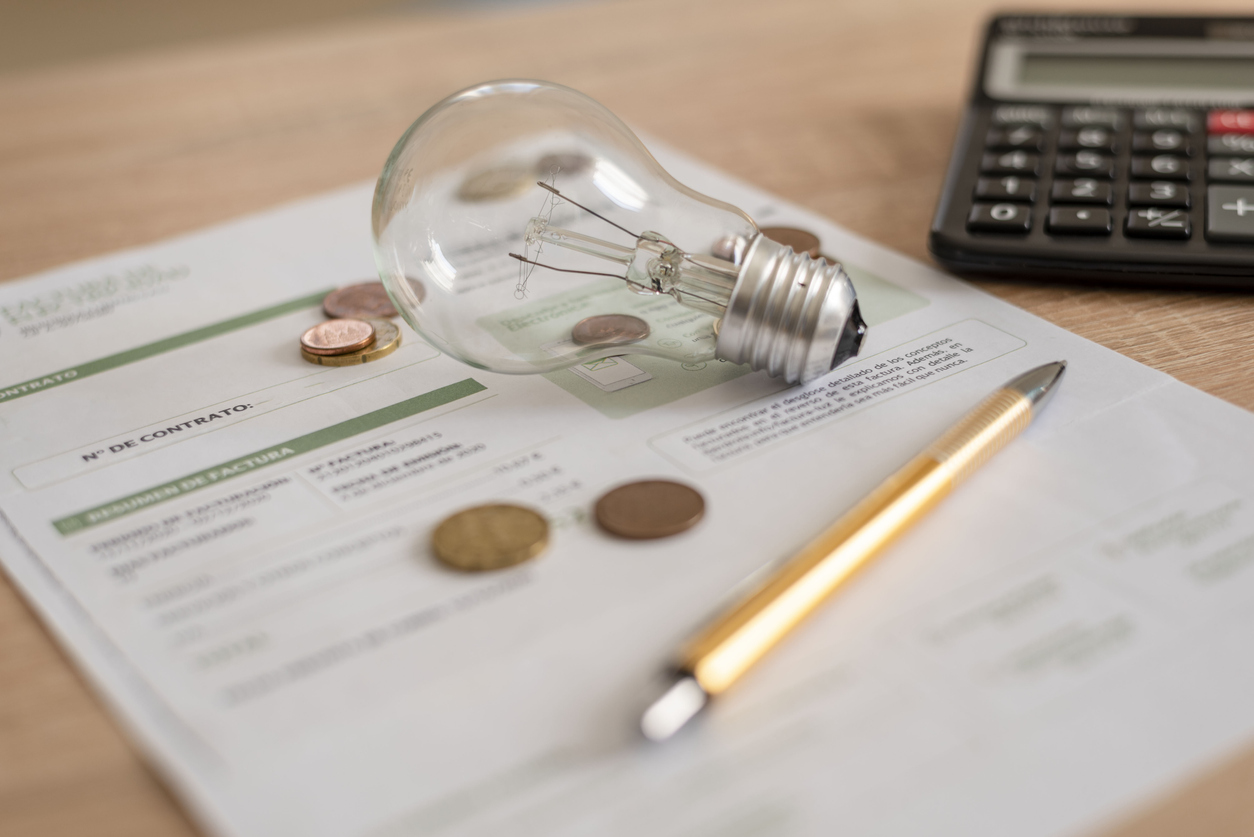 Electricity bill with light bulb, several coins, calculator and pen on the desk. Concept of electricity prices and tax payments