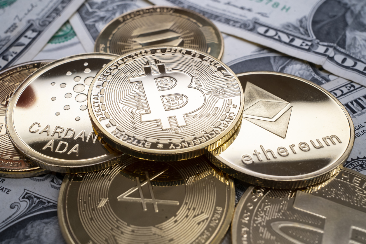 A selection of different cryptocurrency coins piled together over US dollar banknotes