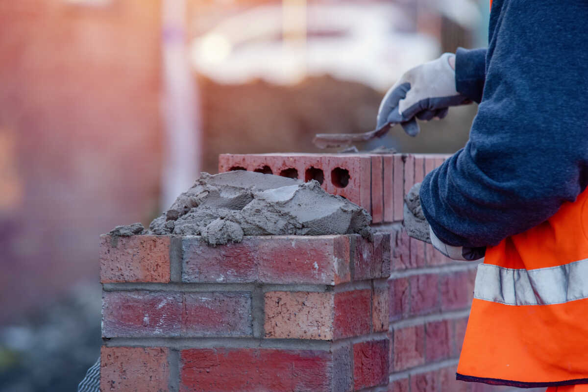 Close up of industrial bricklayer laying bricks on cement mix on construction site