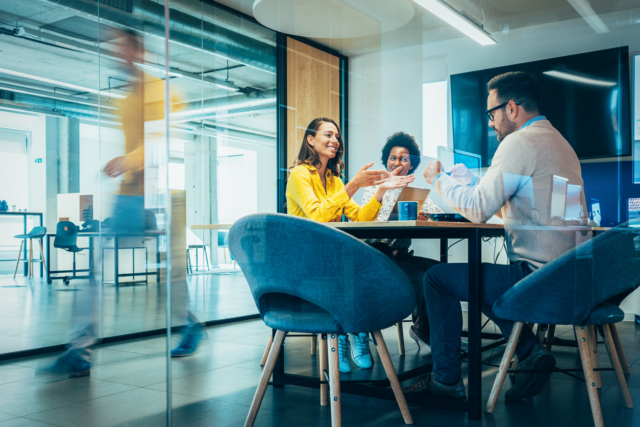 Businesspeople in Conference Room and Colleagues Walking By. Blurred motion of colleagues walking briskly down office hallway as colleagues sit in conference room discussing ideas. Busy modern workplace. Working process in the office, business people working, walking and talking, blurred motion