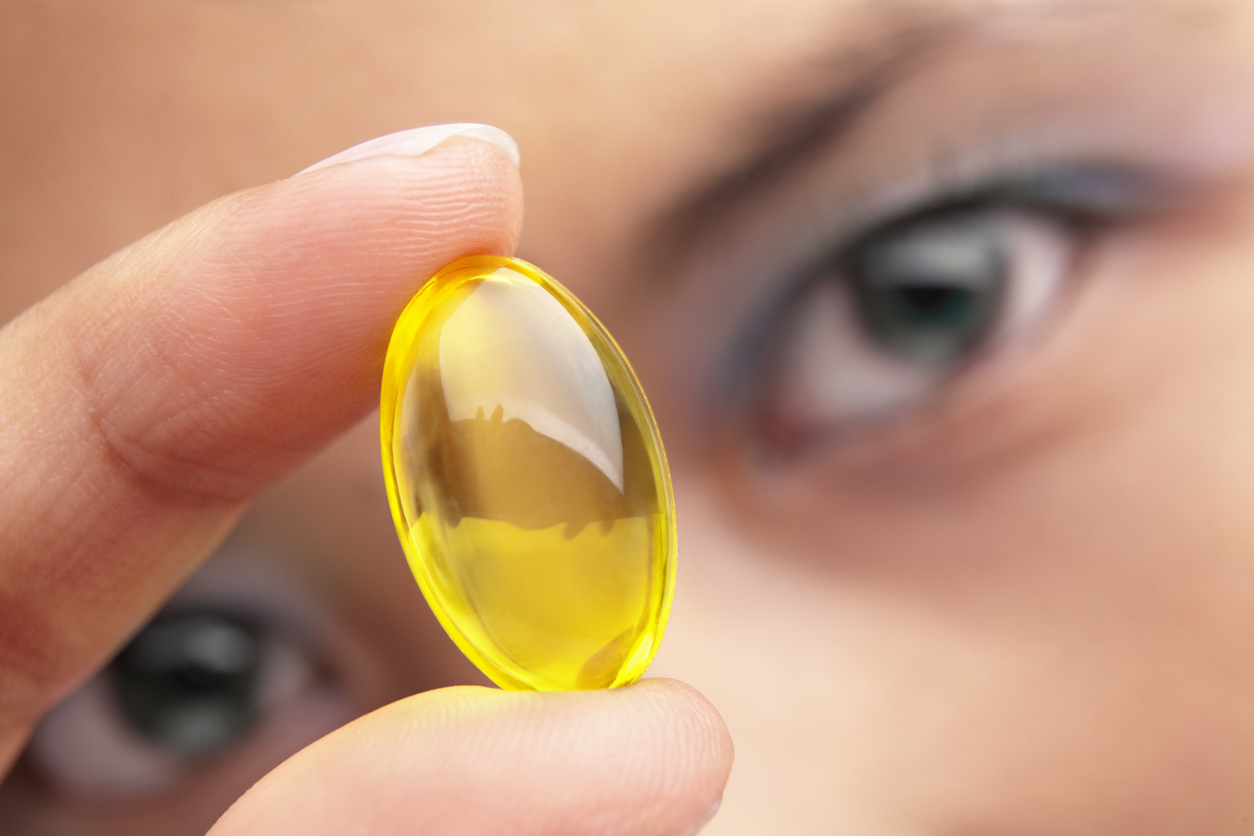 A woman holding a yellow vitamin capsule, close up