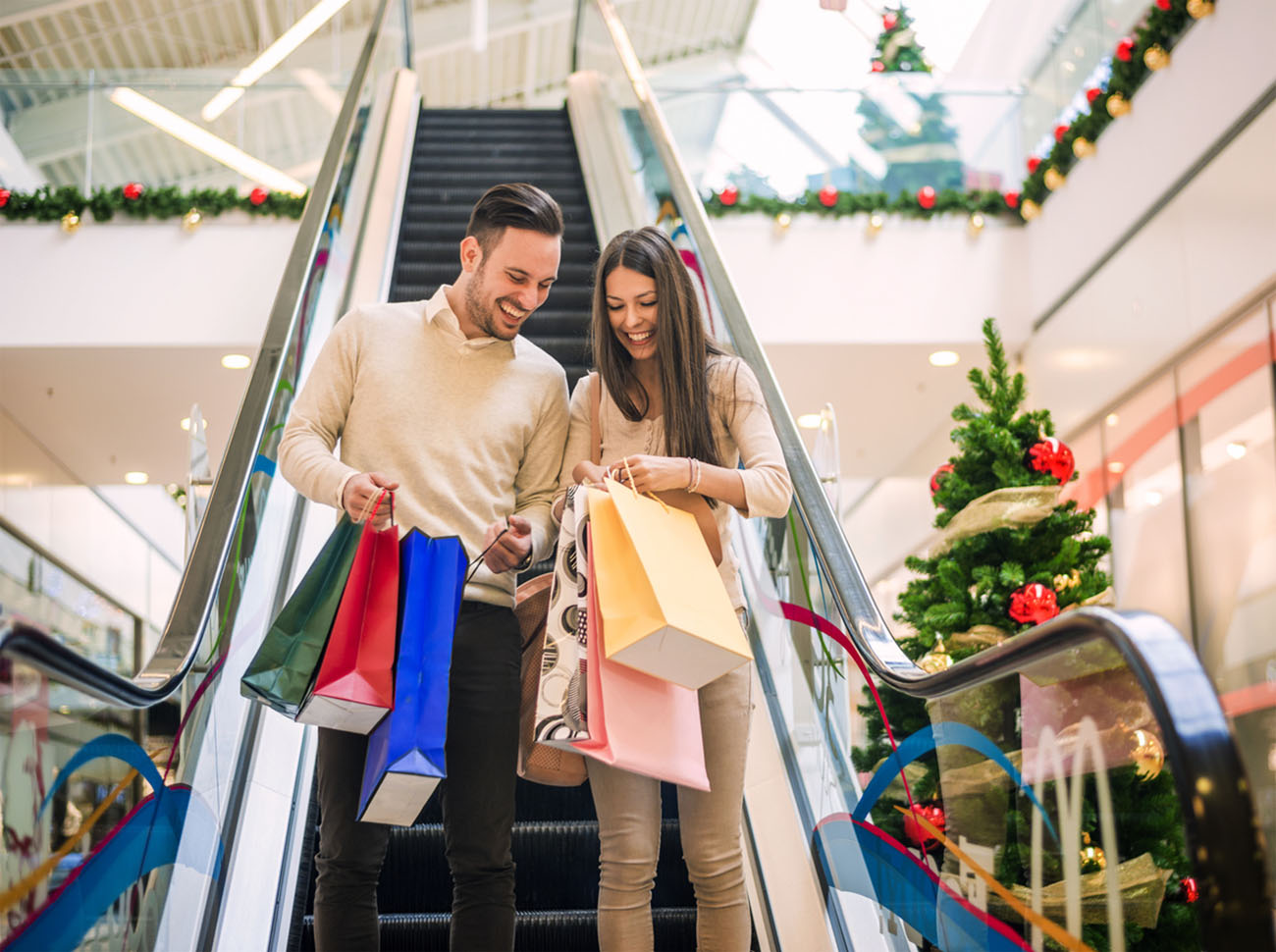 Romantic Christmas shopping.Sale, technology and people concept - happy young couple with shopping bags.Image taken inside a shopping mall.