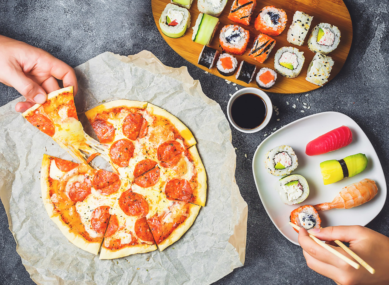 Tasty Pizza with salami, set of sushi rolls and hands take food. Dark background. Flat lay, top view.