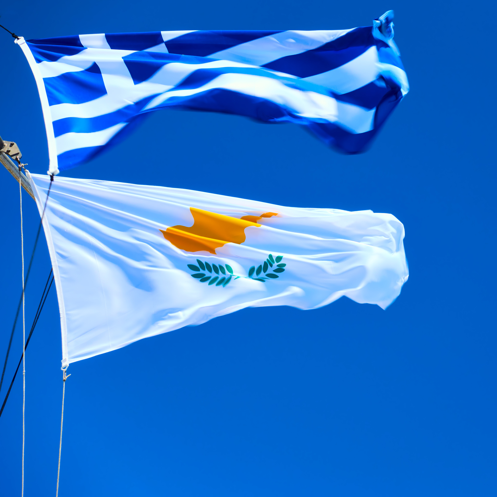 Waving Greek and Cyprian flags agaist the blue sky in strong wind