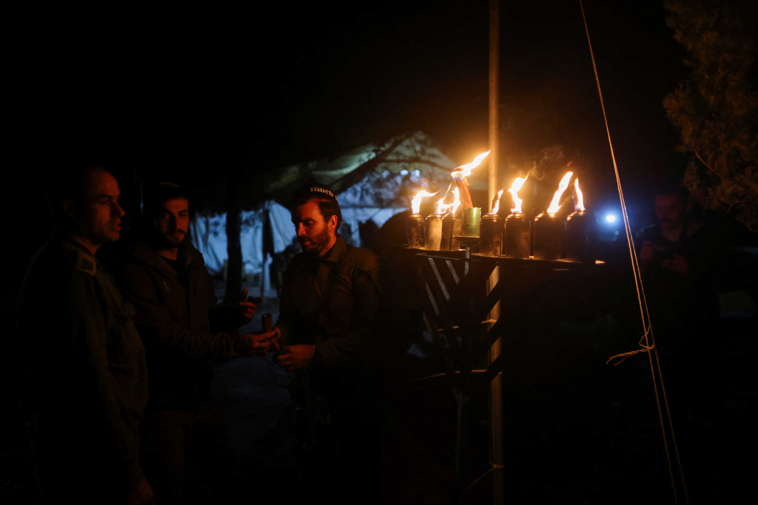Israeli soldiers light the candles of a Hanukkiyah, a candlestick with nine branches that is lit to mark the Jewish holiday of Hanukkah, amid the ongoing conflict between Israel and the Palestinian Islamist group Hamas, near Israel's border with Gaza in southern Israel December 13, 2023. REUTERS