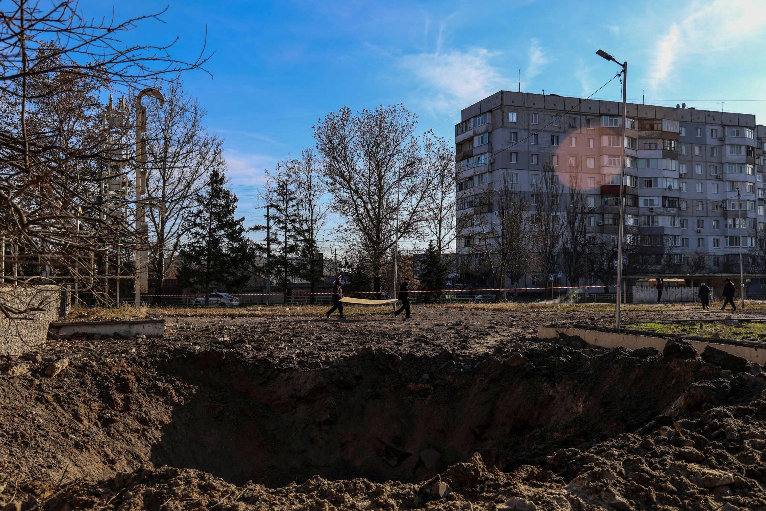 Local residents carry an OSB panel next to a crater from a Russian missile strike, amid Russia's attack on Ukraine, in Kherson, Ukraine December 5, 2023. REUTERS