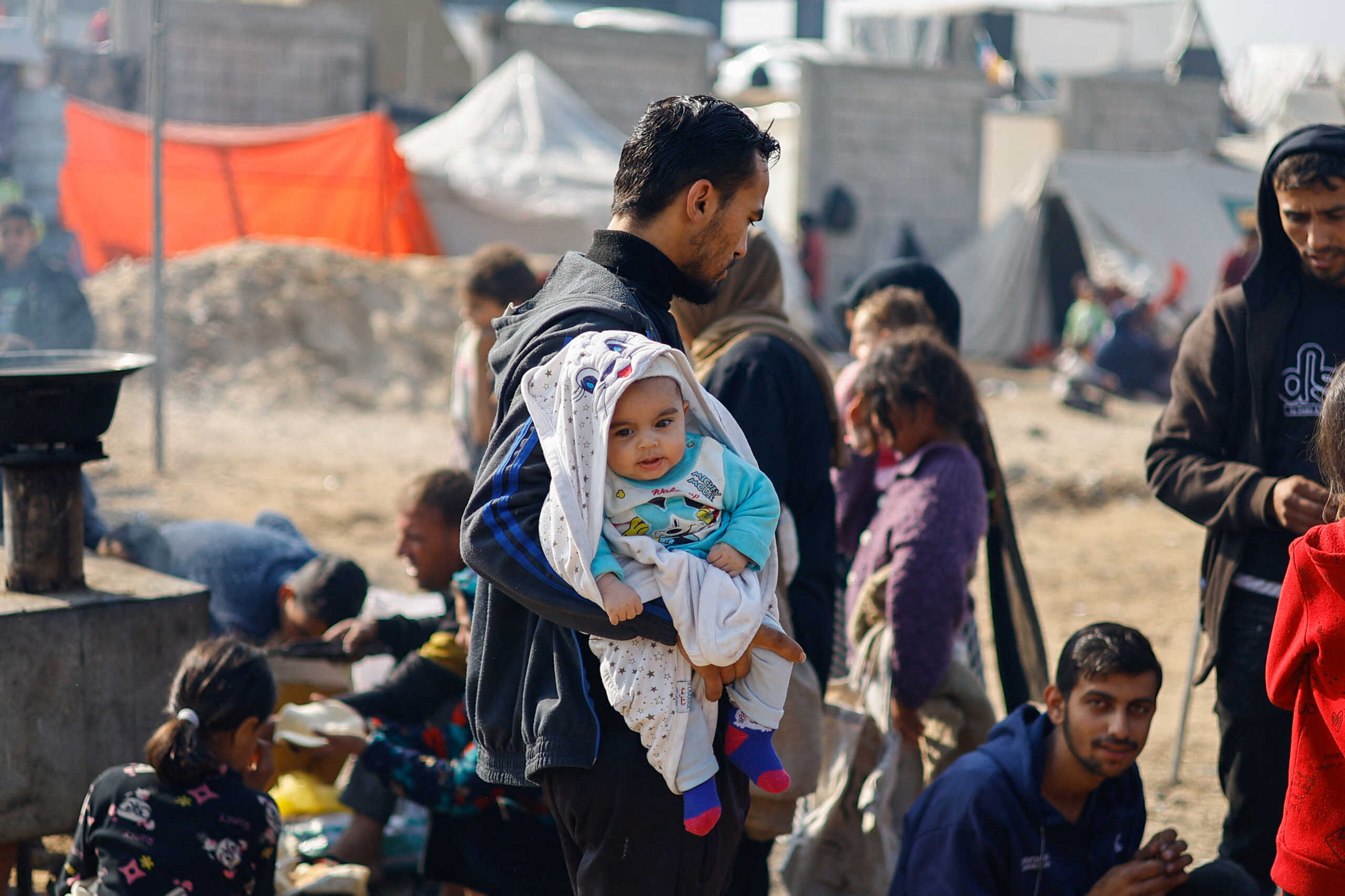 A man holds a baby as displaced Palestinians, who fled their homes due to Israeli strikes, shelter in a tent camp, amid the ongoing conflict between Israel and the Palestinian Islamist group Hamas, in Rafah, southern Gaza Strip, January 1, 2024. REUTERS