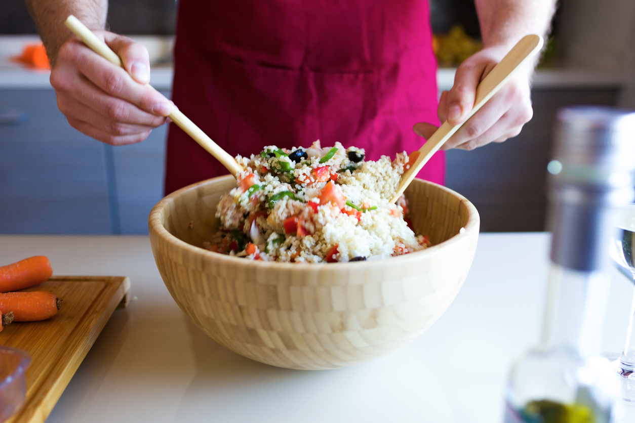 Close-up of handsome young man preparing quinoa salad with vegetables in the kitchen.