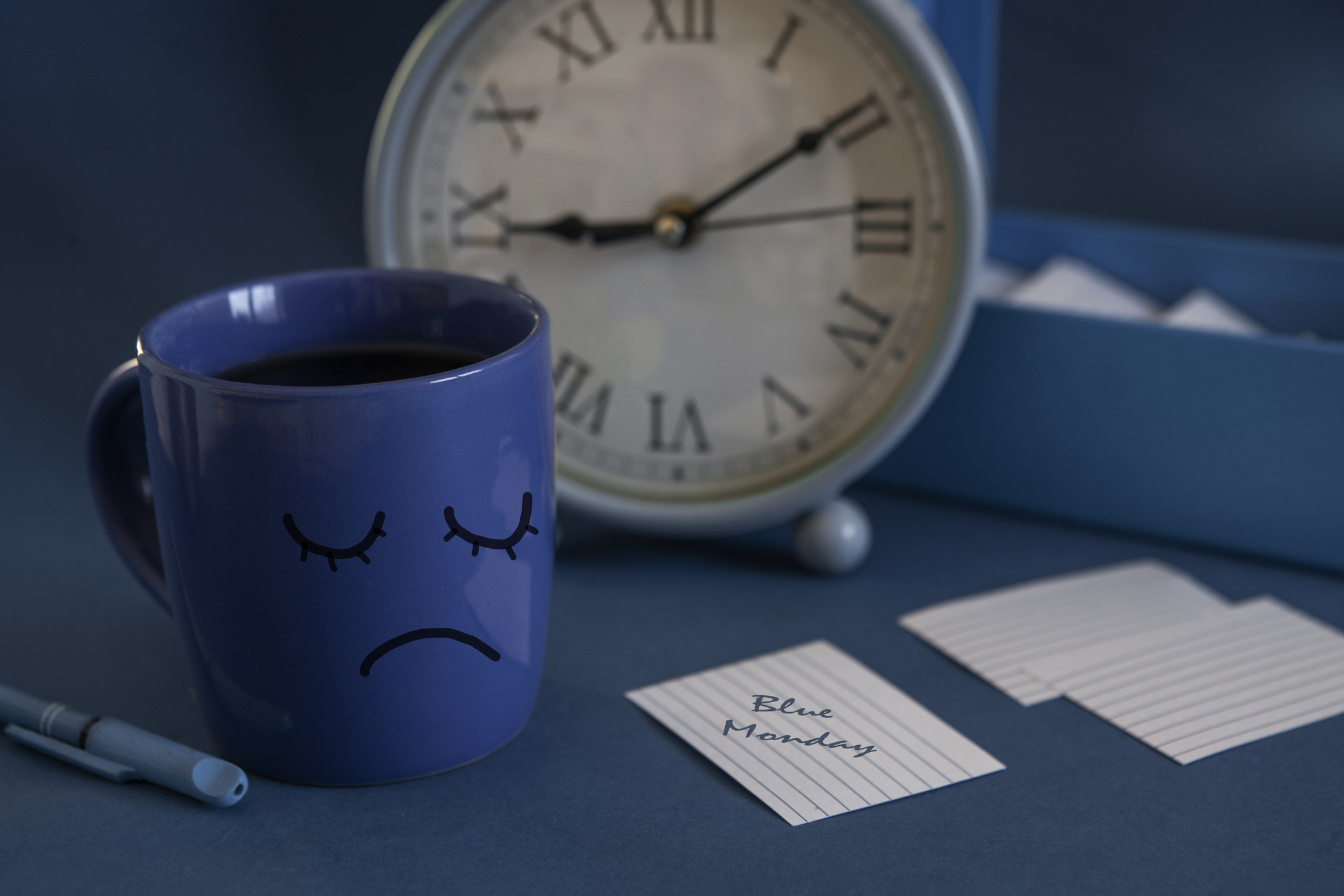 The beginning of the working day on blue Monday. Cup of tea, alarm clock and a note with the text Blue Monday. The most depressed day of the year