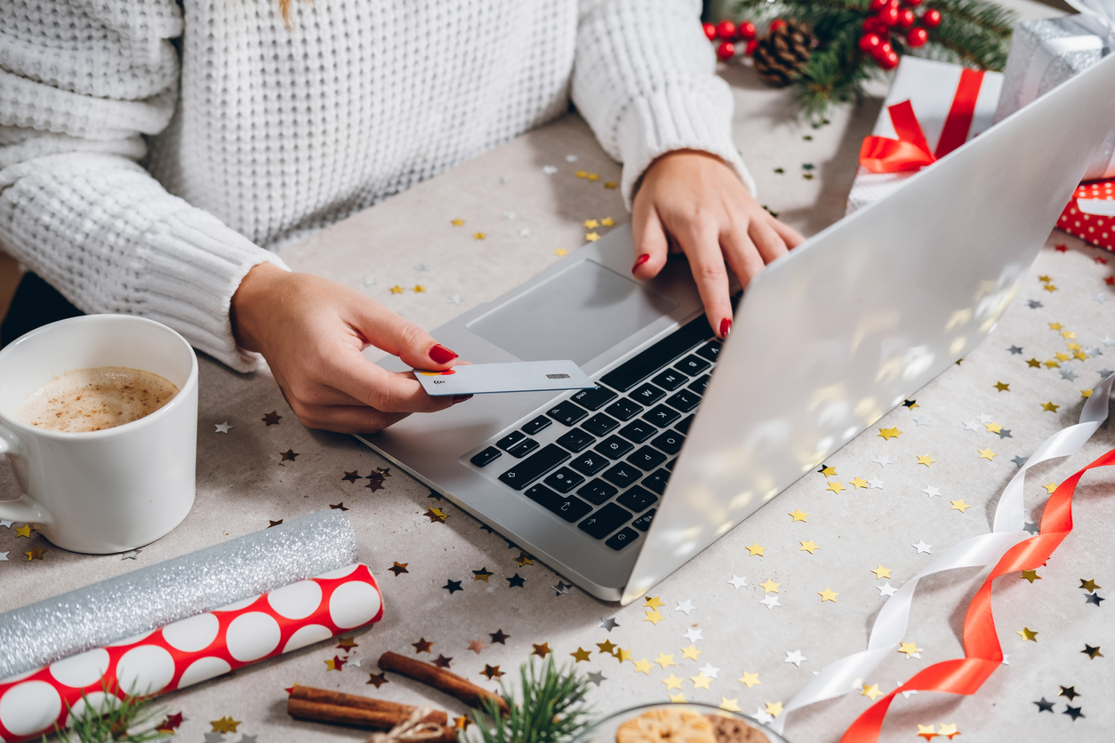 Christmas online shopping top view. Woman buying presents online with silver credit card and laptop computer, drinks coffee among gift boxes. Winter holidays sales concept