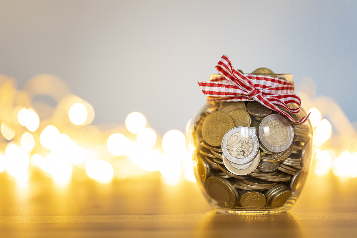Savings jar full of coins in front of the Christmas lights. Coins saved for holiday expenses.