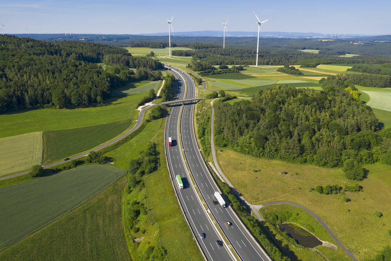 Multiple lane highway with trucks in rural area, wind turbines in the background, bird's eye view.