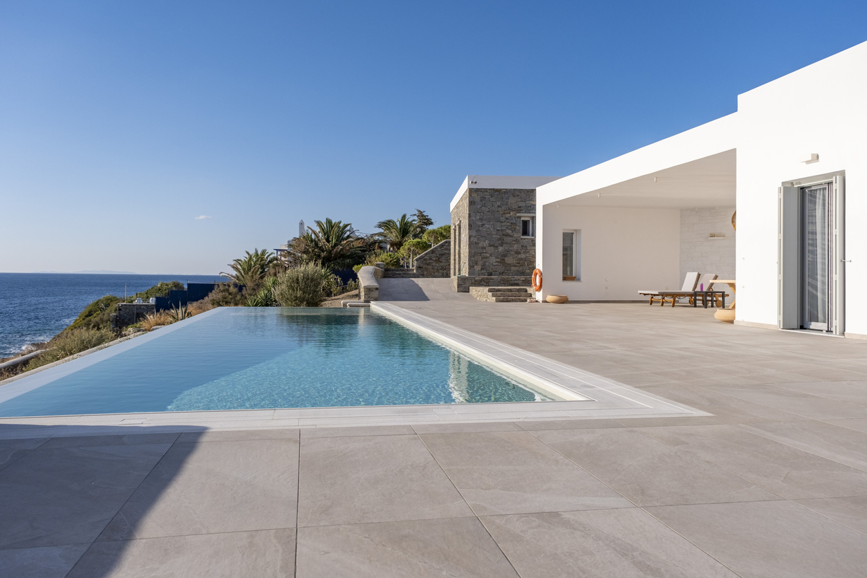 Luxury modern minimalist house exterior with infinity swimming pool and beautiful sea and ocean view. Poster template background for Real estate, tourism hotel, home and villa vacation rental with large copy space.