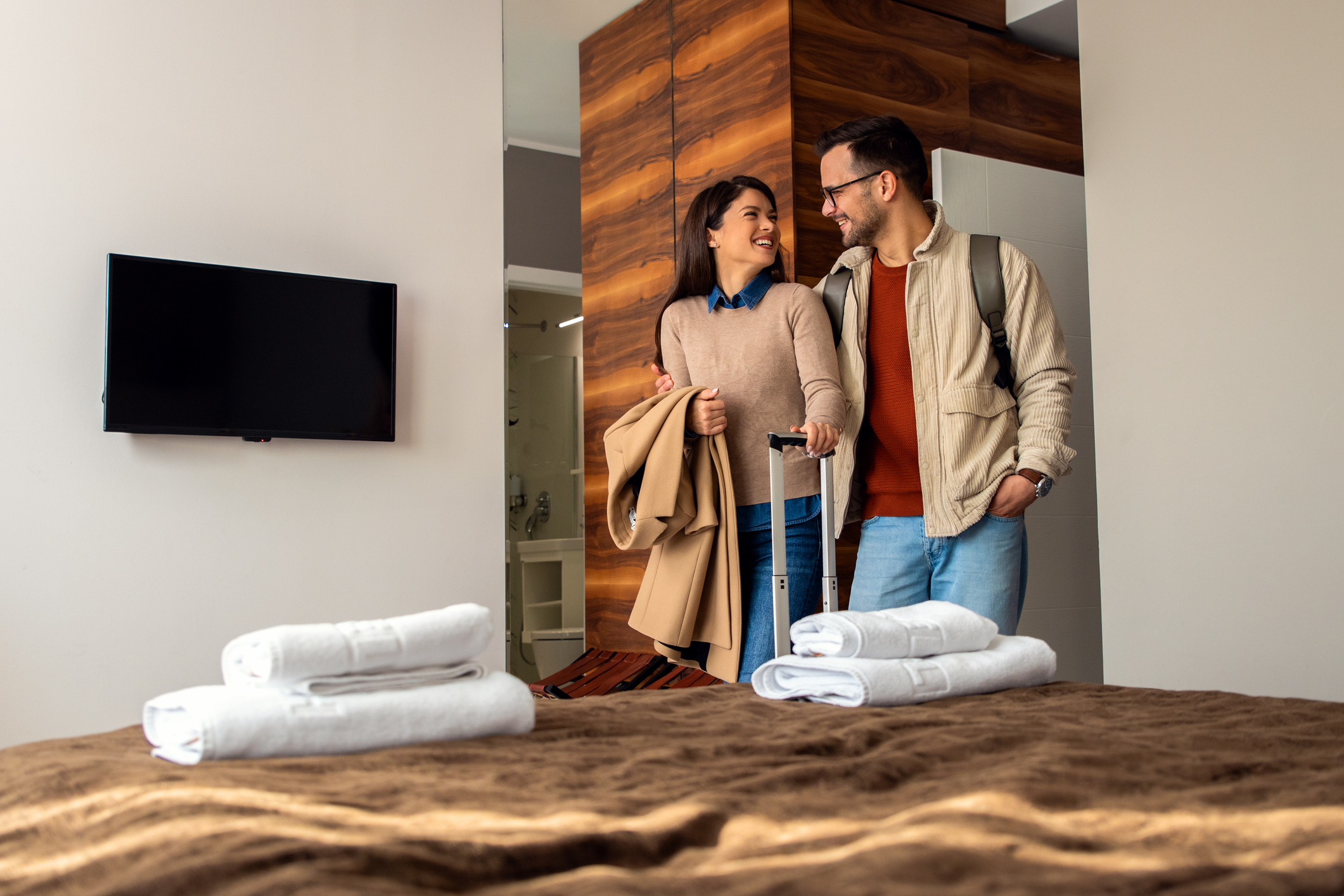 Smiling couple with suitcase arriving in hotel room.