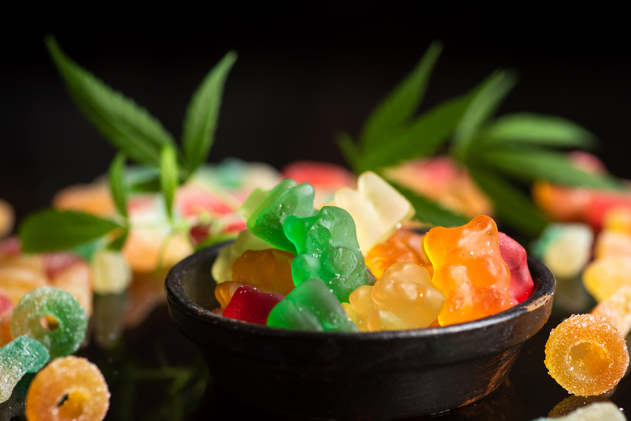 Colored gum candy jelly with marijuana leaves, on a black glass background. Sweet gummy candy with CBD, THC oil.