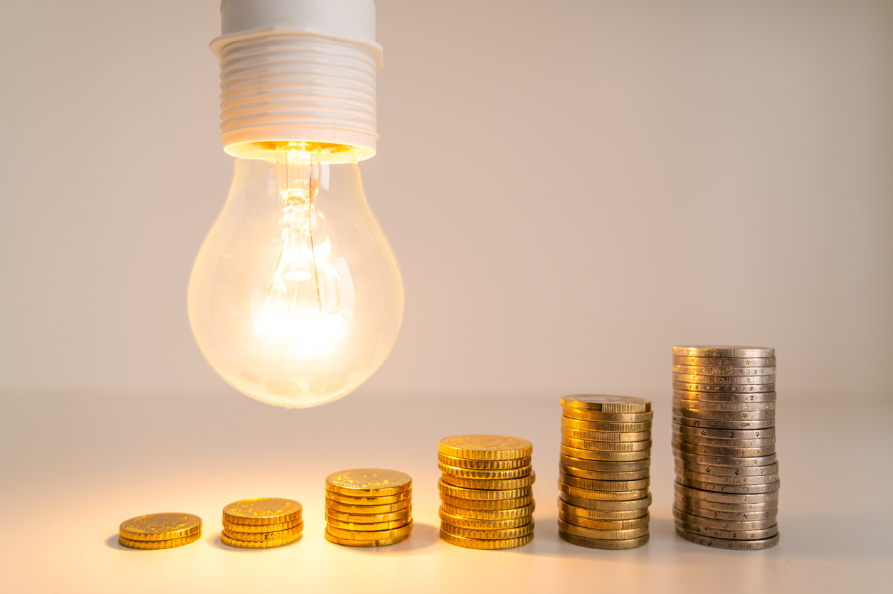 Lit light bulb with coins beside it. Increase in energy tariffs. Efficiency and energy saving.
