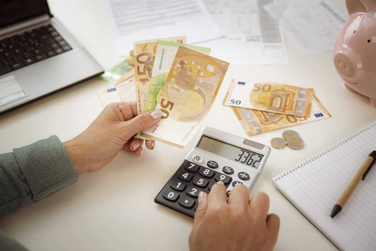 Close-up of woman's hands using calculator for planning home finances. She is holding Euro banknotes.