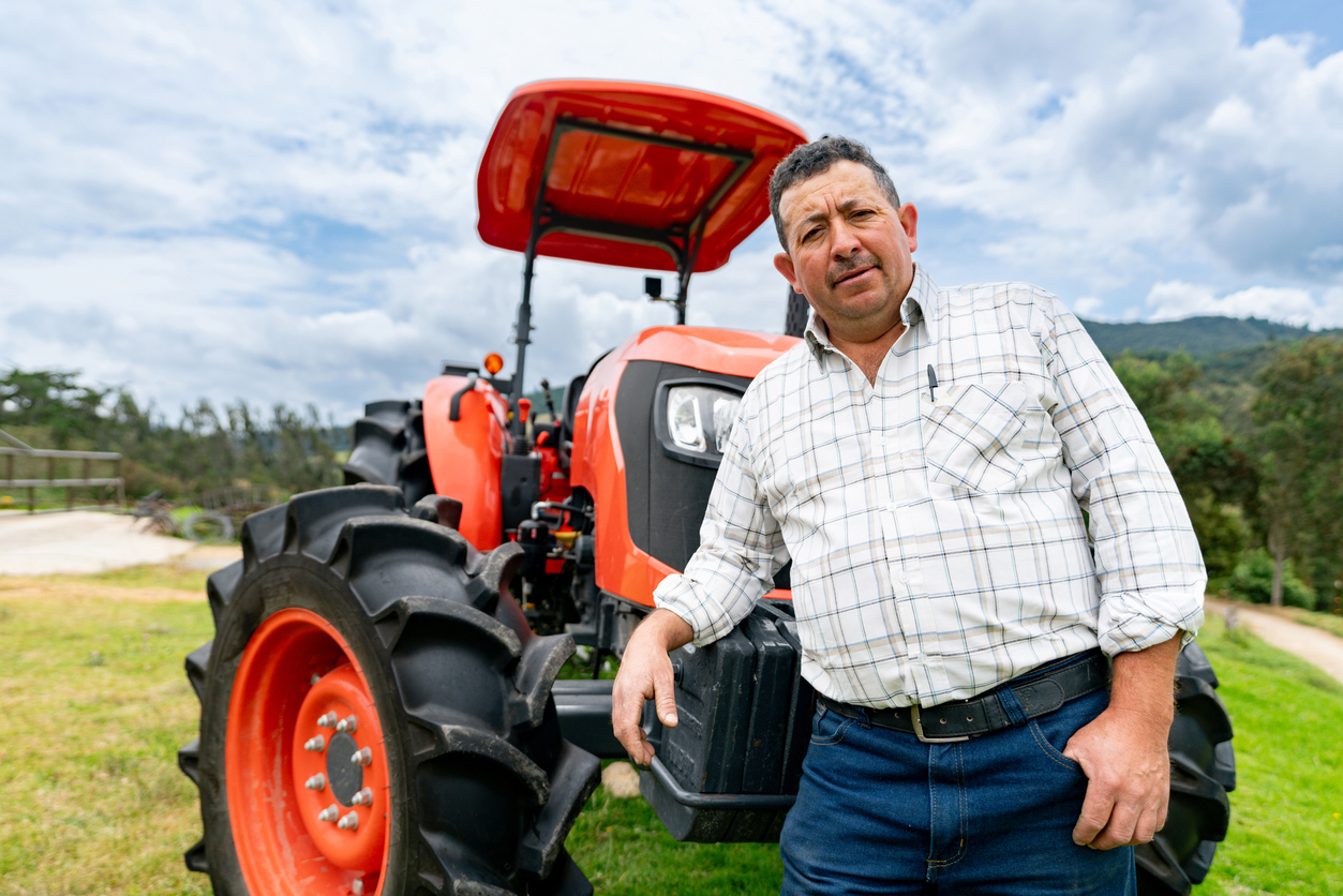 Portrait of a Latin American farmer leaning against his tractor outdoors and looking at the camera - agriculture concepts