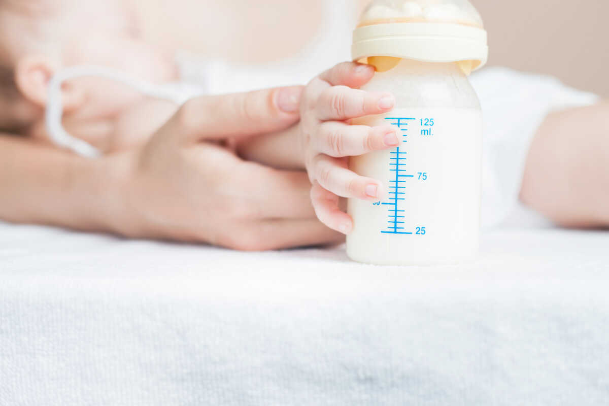Baby holding a baby bottle with breast milk for breastfeeding. Mothers breast milk is the most healthy food for newborn baby. There is empty blank billboard and copy space for text and design