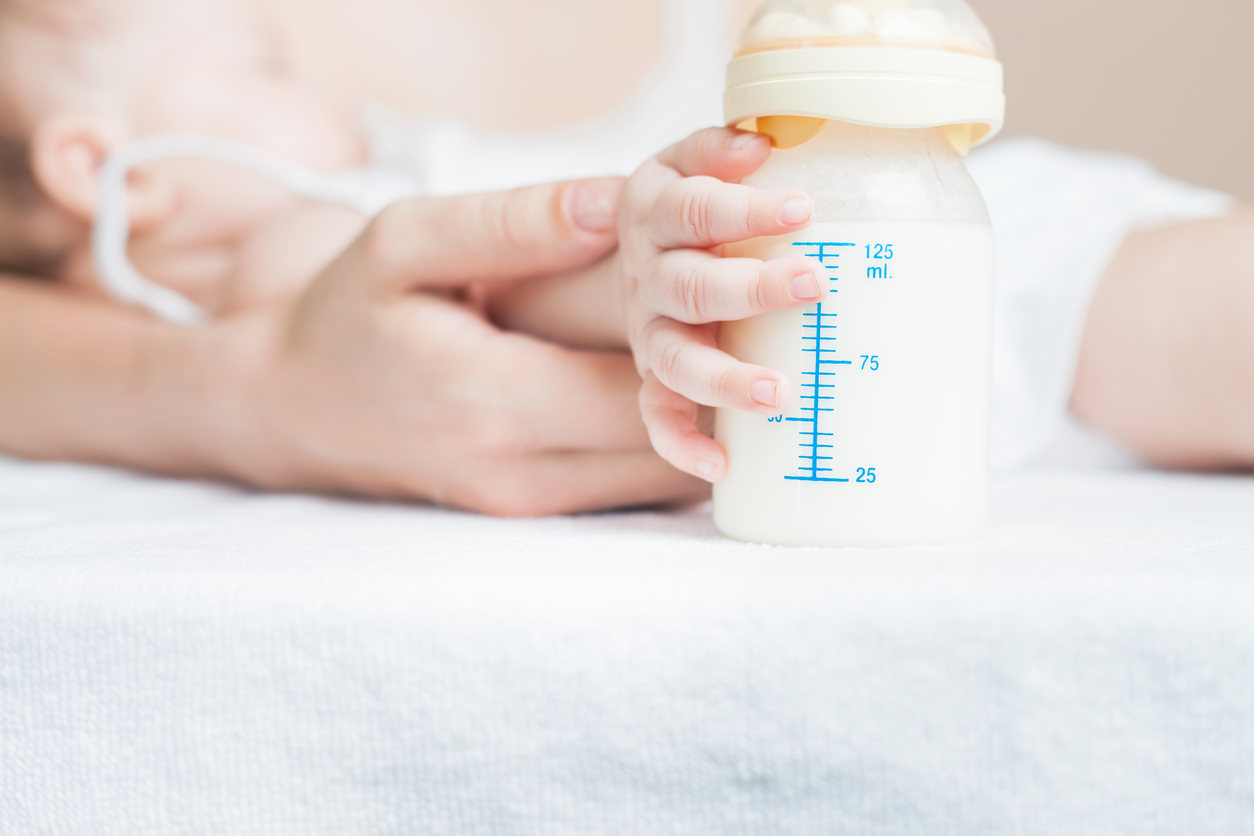 Baby holding a baby bottle with breast milk for breastfeeding. Mothers breast milk is the most healthy food for newborn baby. There is empty blank billboard and copy space for text and design