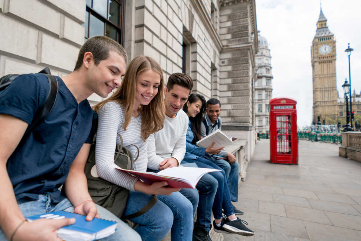 Happy group of students in London studying outdoors reading notes on their notebooks - education concepts
