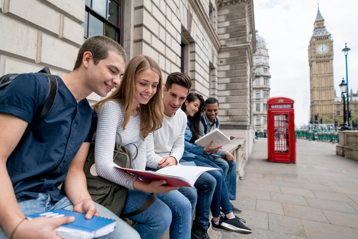 Happy group of students in London studying outdoors reading notes on their notebooks - education concepts