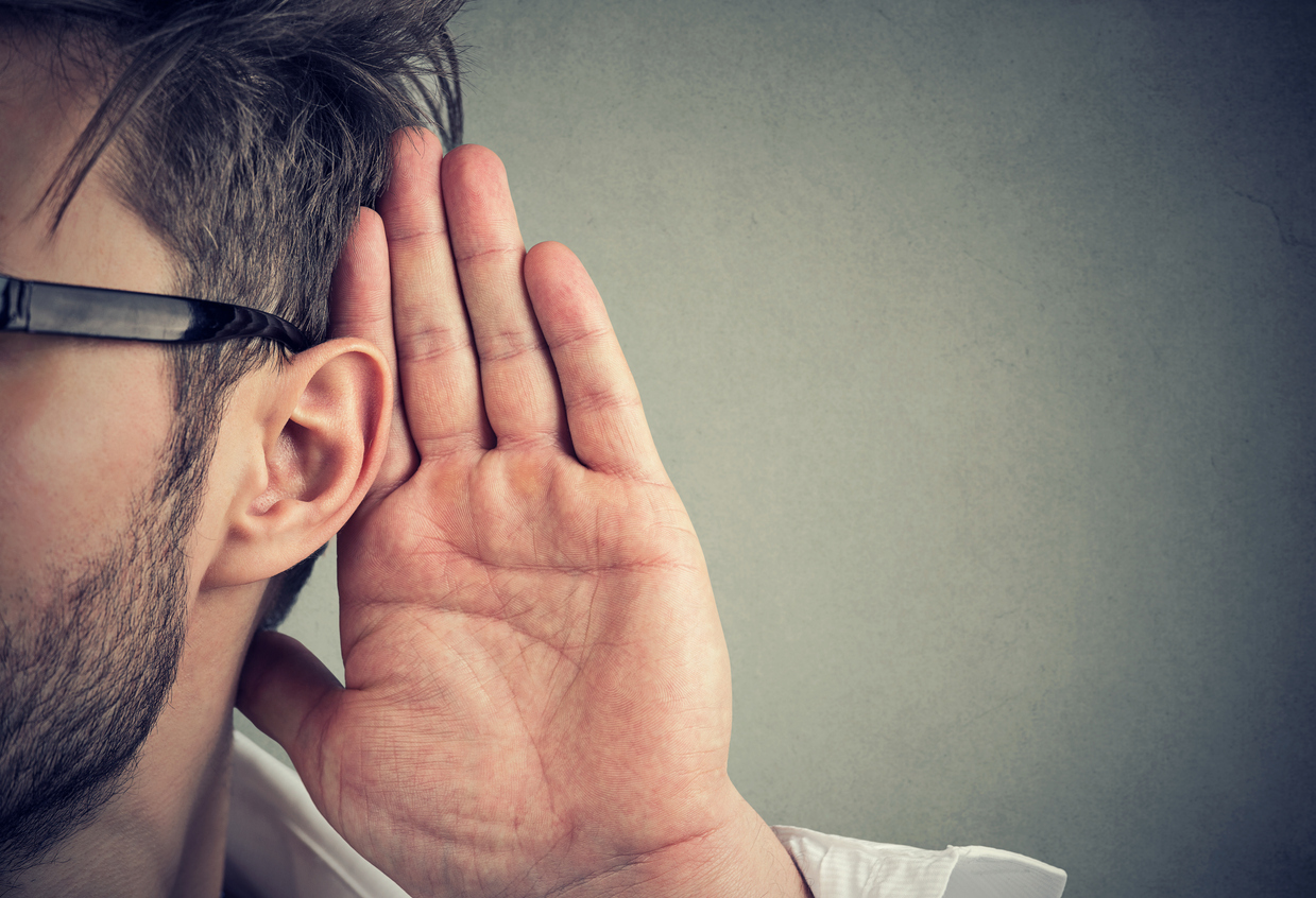 man holds his hand near ear and listens carefully isolated on gray wall background
