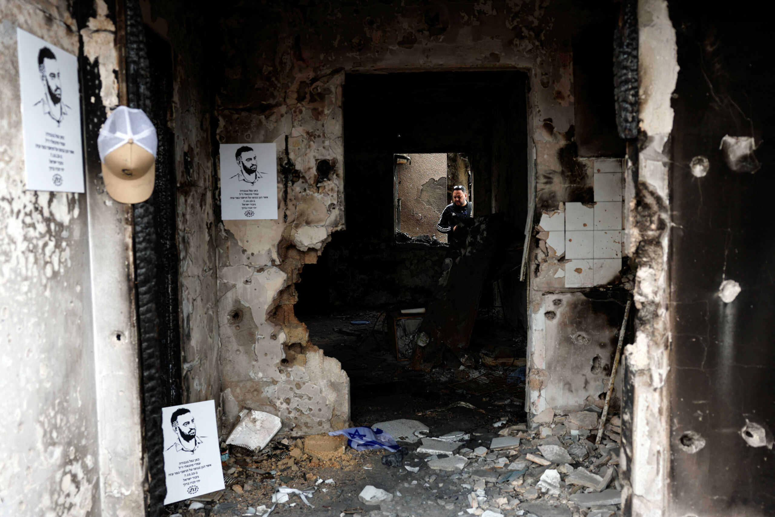 A man looks through the window at the remains of a home where Omri Michaeli was killed during the deadly October 7 attack by gunmen from Palestinian Islamist group Hamas, at Kibbutz Kfar Aza in southern Israel January 3, 2024. The posters on the wall depict Omri. REUTERS