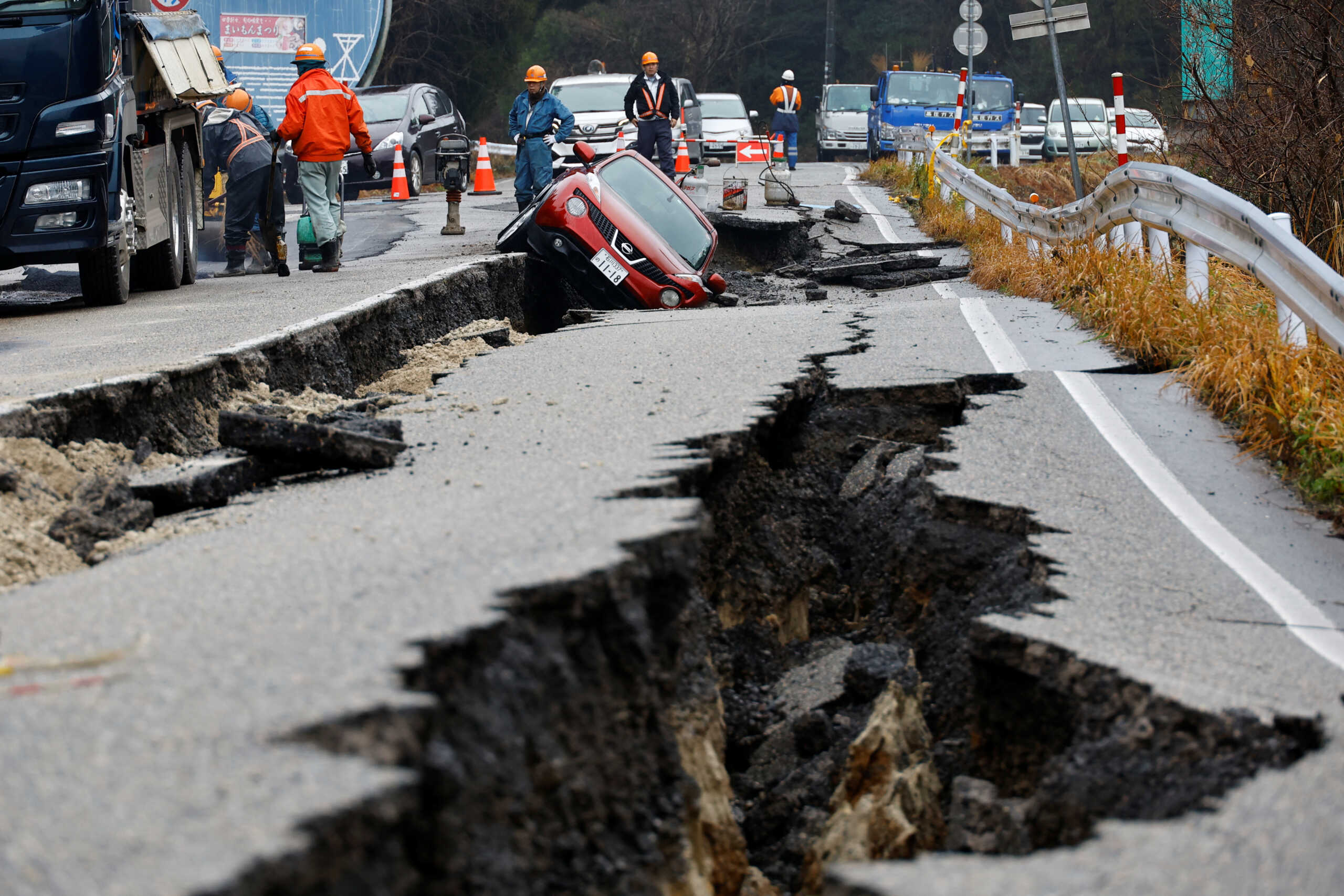 Workers repair a road next to a car stuck on a broken road, in the aftermath of an earthquake, near Anamizu, Japan, January 3, 2024. REUTERS