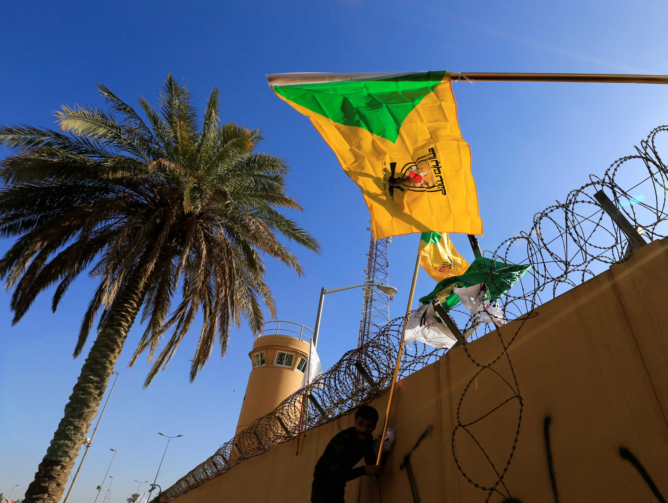 FILE PHOTO: A member of Hashd al-Shaabi (paramilitary forces) holds a flag of Kataib Hezbollah militia group during a protest to condemn air strikes on their bases, outside the main gate of the U.S. Embassy in Baghdad, Iraq December 31, 2019. REUTERS