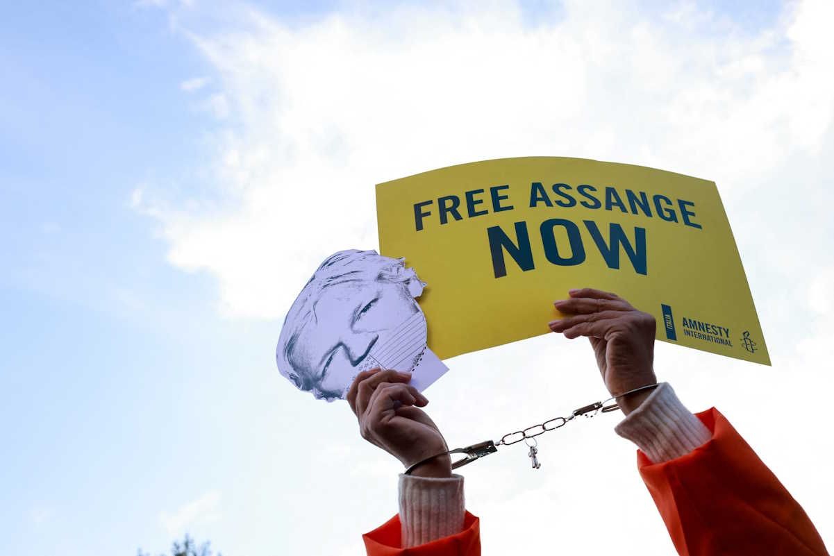 A handcuffed person holds a placard and a mask depicting WikiLeaks founder Julian Assange, as his supporters demonstrate in front of the British Embassy, claiming to stop Assange's extradition from Britain to the United States, in Rome, Italy, February 20, 2024. REUTERS