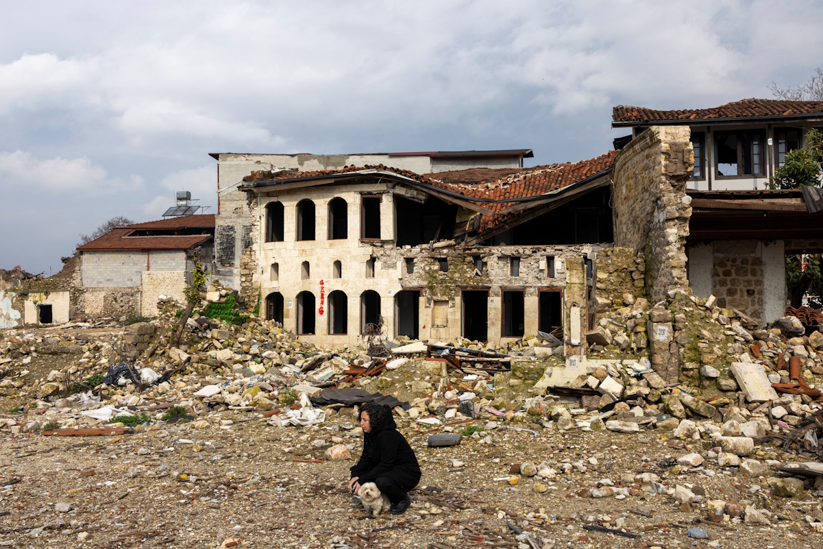 A woman looks on as she squats with a dog beside houses destroyed by last year's earthquake, in Hatay, Turkey, February 5, 2024. The magnitude 7.8 tremor that struck in the early hours of Feb. 6, 2023, levelled towns and city swathes in the country's southeast. It killed more than 53,000 people in Turkey and nearly 6,000 in neighbouring Syria and left millions homeless. REUTERS