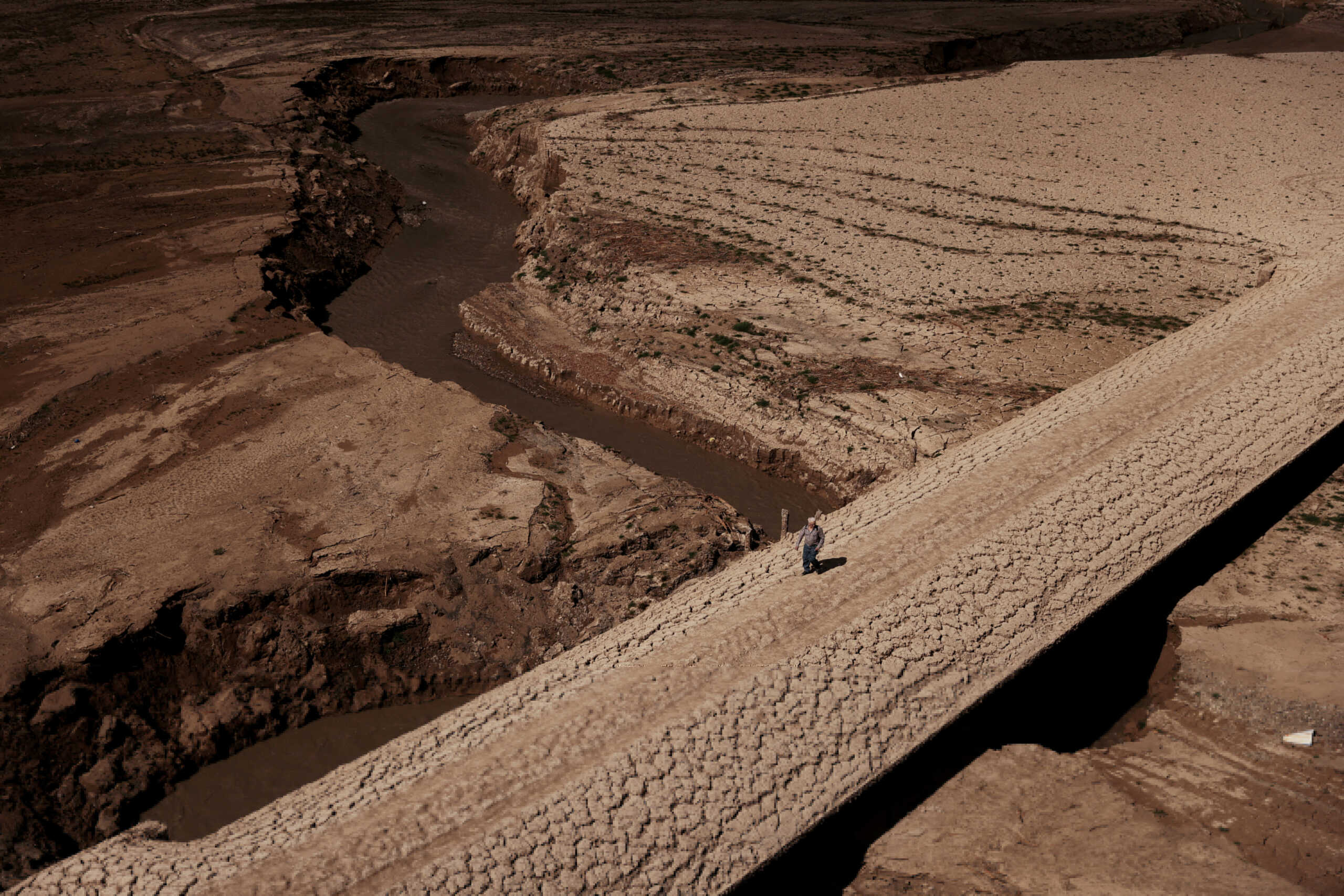 FILE PHOTO: A man walks on the cracked ground of the Baells reservoir as drinking water supplies have plunged to their lowest level since 1990 due to extreme drought in Catalonia, in the village of Cersc, in the region Bergueda, Spain March 14, 2023. REUTERS