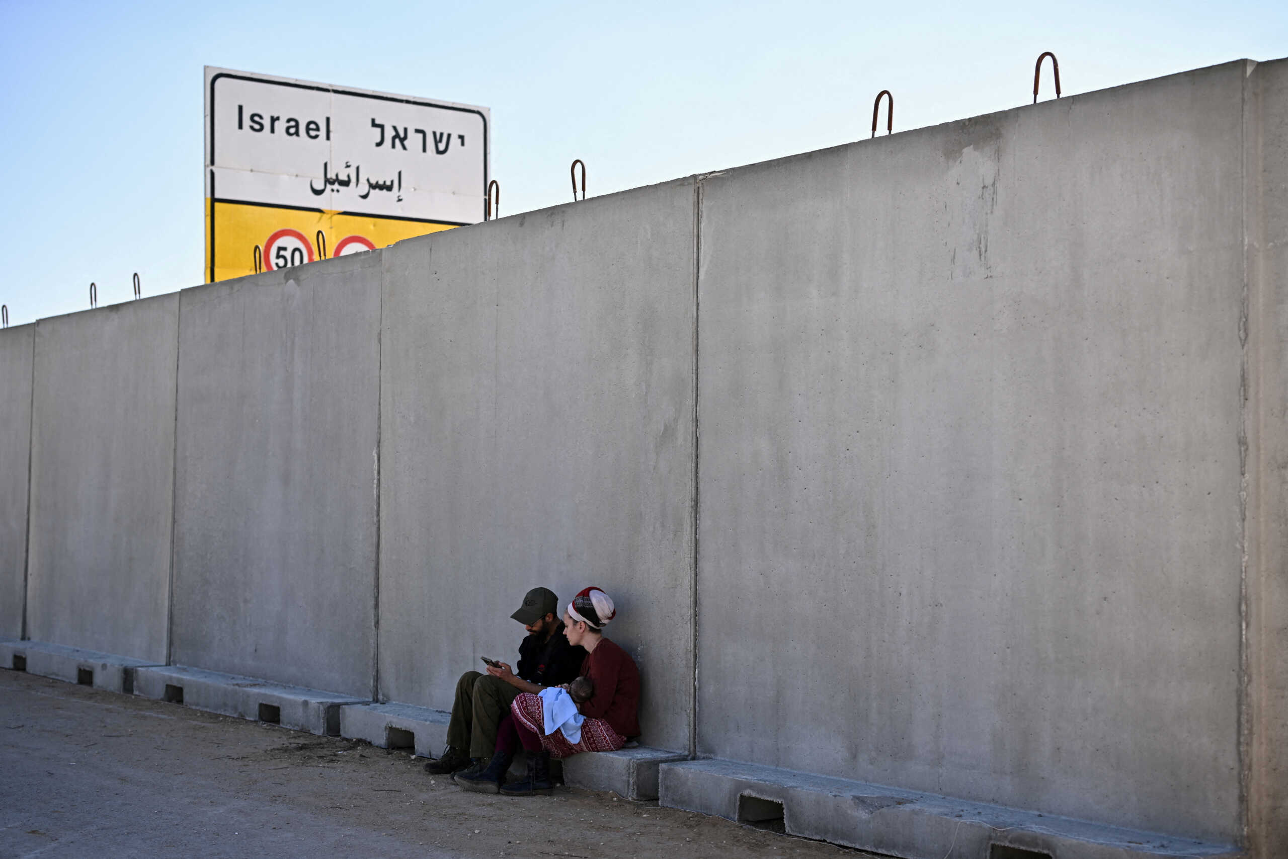 A woman holds a child as they sit by a wall, during a protest against the delivery of humanitarian aid to Gaza and demand the immediate release of hostages kidnapped on the deadly October 7 attack by Palestinian Islamist group Hamas, at the Kerem Shalom crossing, Israel, February 7, 2024. REUTERS