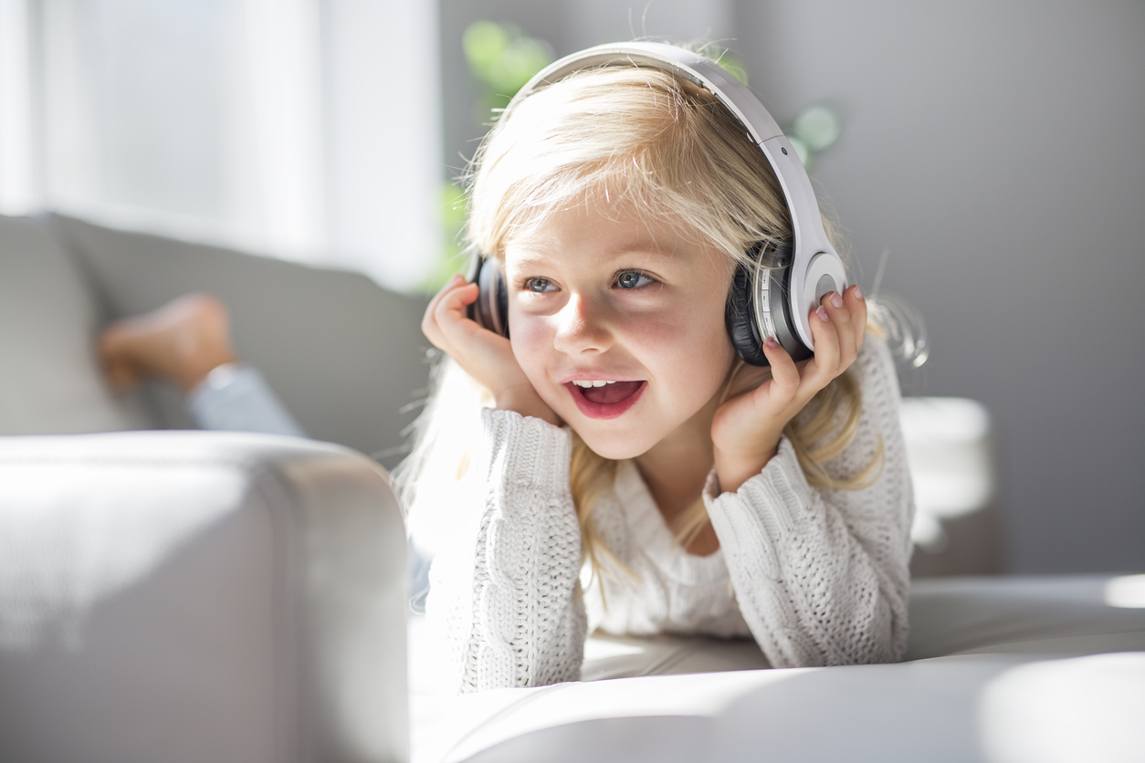 A Happy little girl listening music lying on the sofa living-room
