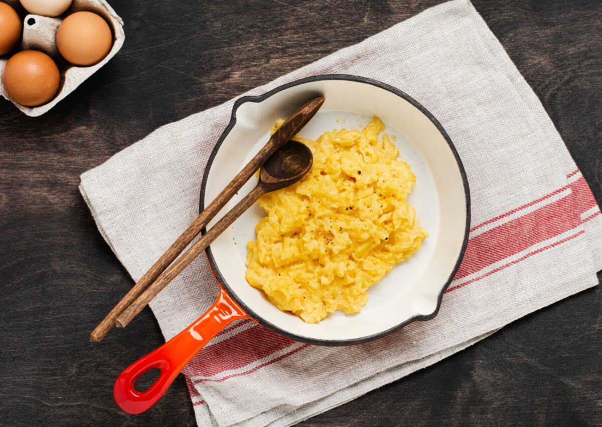 Scrambled eggs for breakfast on frying pan, dark wooden table background. Traditional English breakfast.Top view with cope space.