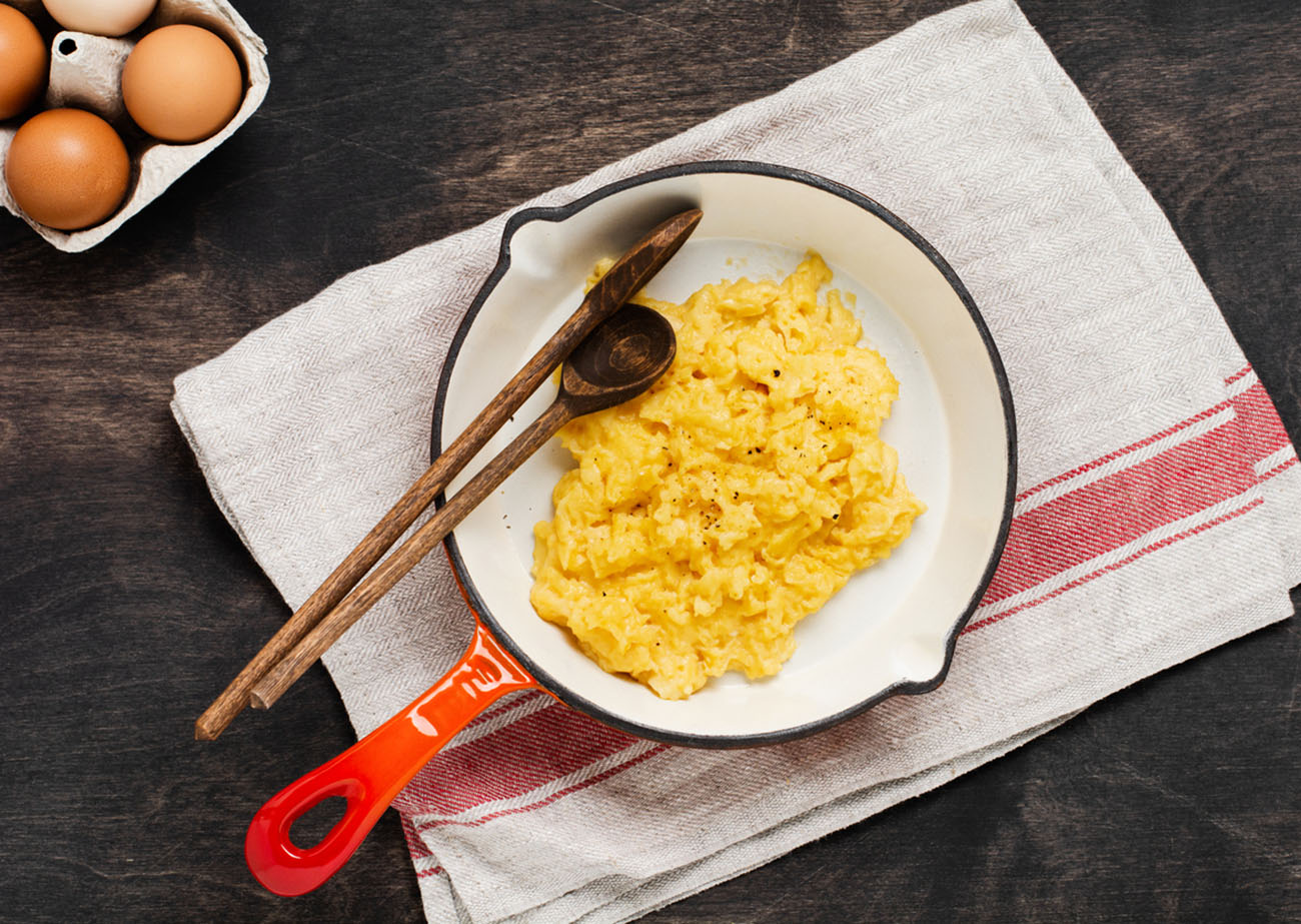 Scrambled eggs for breakfast on frying pan, dark wooden table background. Traditional English breakfast.Top view with cope space.