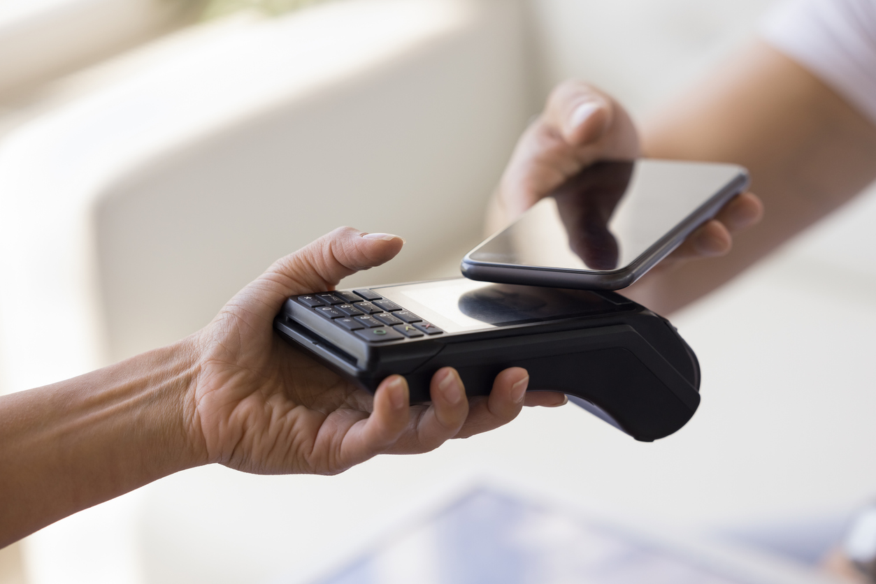 Female hand holding POS terminal, offering gadget for customer applying mobile phone, making cashless payment, scanning code, paying bill for purchase. Close up cropped shot