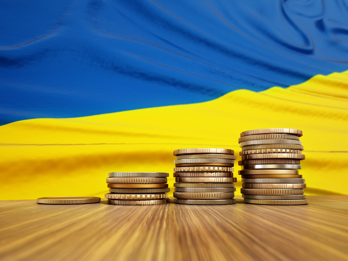 Rising stack of coins with Ukraine flag in the background. Economy, finance, interest rates concept.