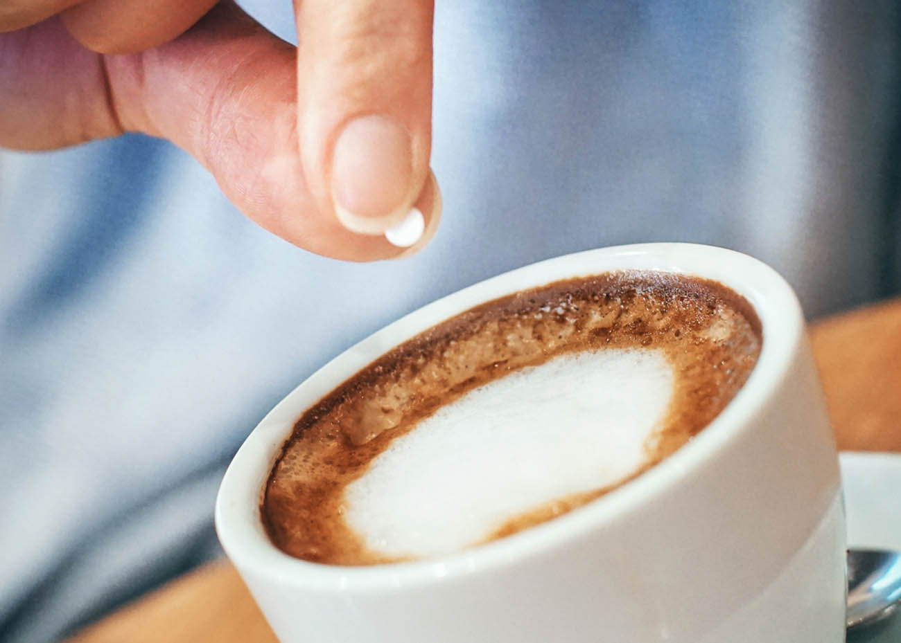 Closeup of unrecognizable woman putting one piece of artificial sweetener into her coffee. These sweeteners are based on aspartame or acesulfam compunds . Tilt shot.