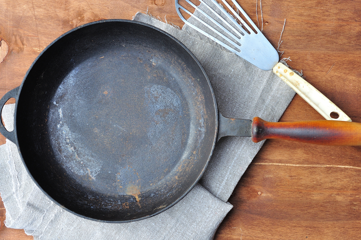 Empty black cast-iron frying pan and iron spatula on the table, top view