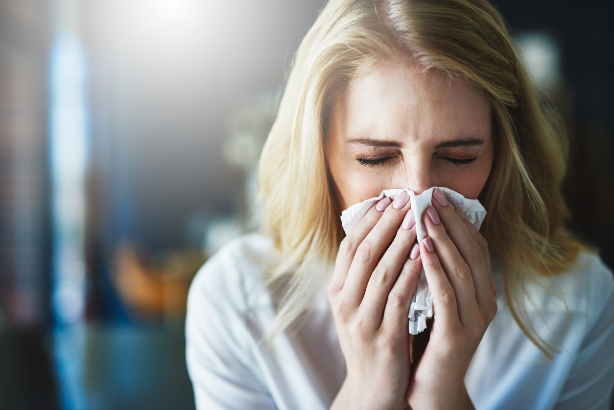 Shot of a frustrated businesswoman using a tissue to sneeze in while being seated in the office