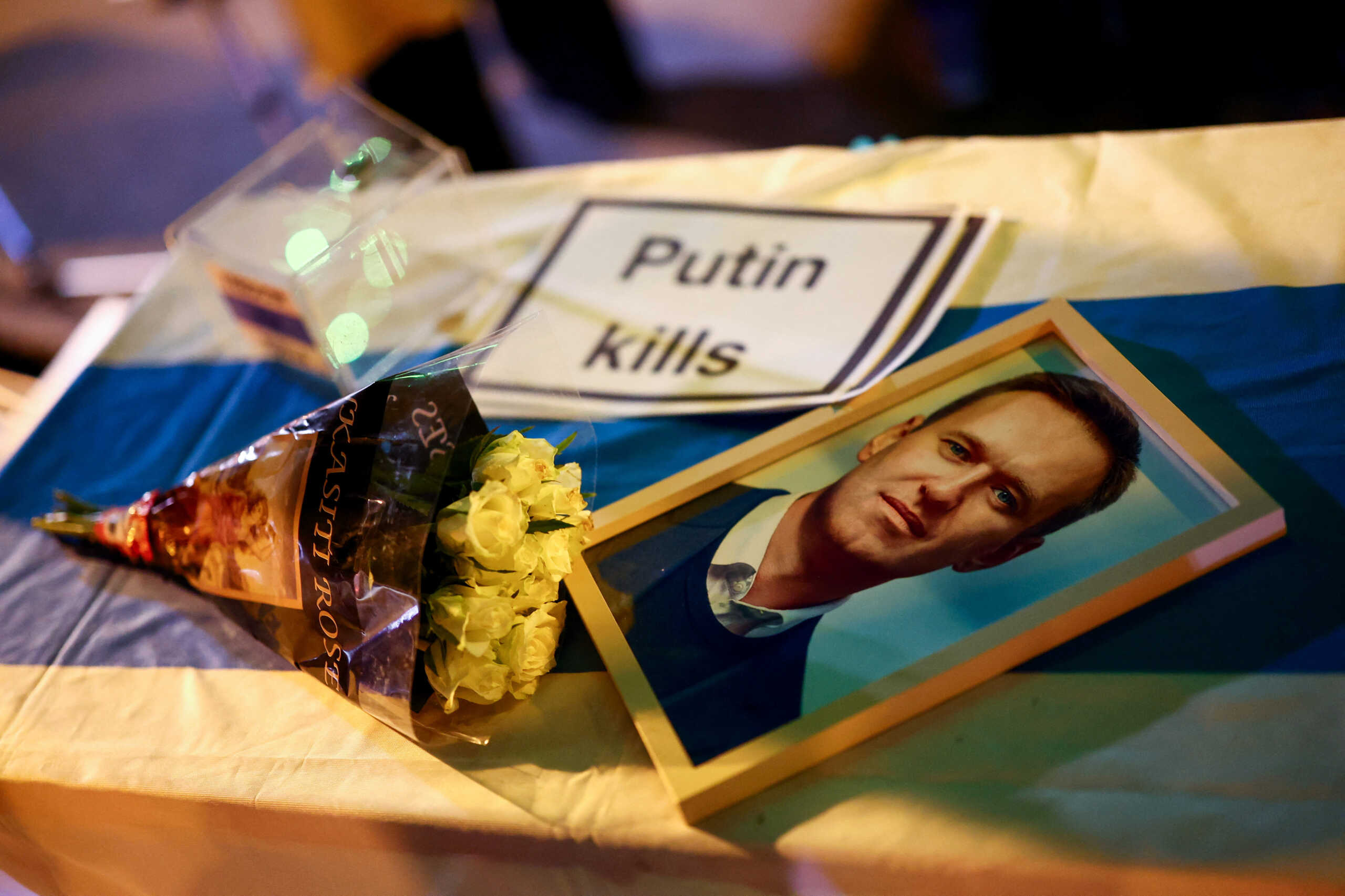 A portrait of opposition leader Alexei Navalny lays on a table next to a sign and flowers as people attend a vigil in memory of Navalny in front of the Russian consulate at Europa square, in Munich, Germany, February 16, 2024. REUTERS