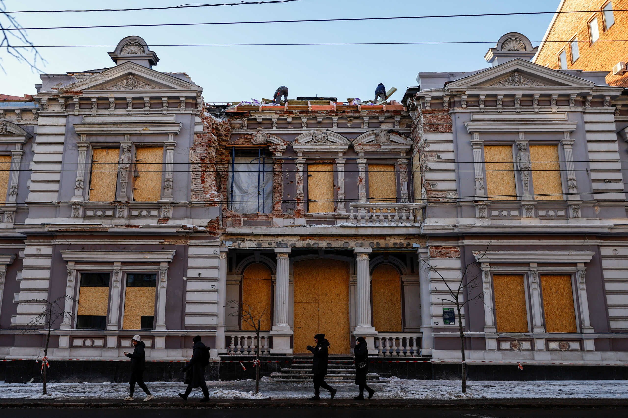 People walk past as workers repair the roof of a historical building, damaged during one of the latest Russian drone strikes, amid Russia's attack on Ukraine, in Kharkiv, Ukraine January 13, 2024. REUTERS